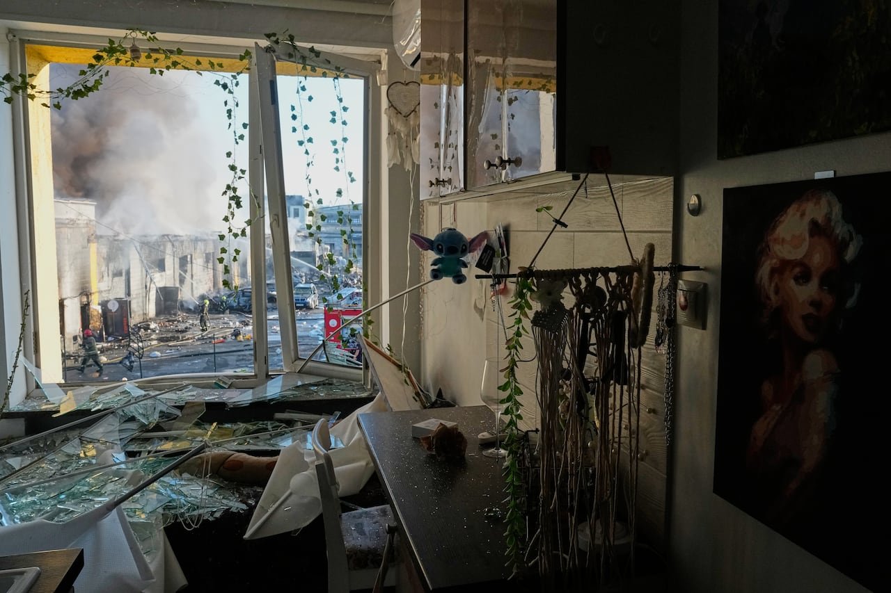 A view from inside a damaged apartment shows debris and fires on the street.