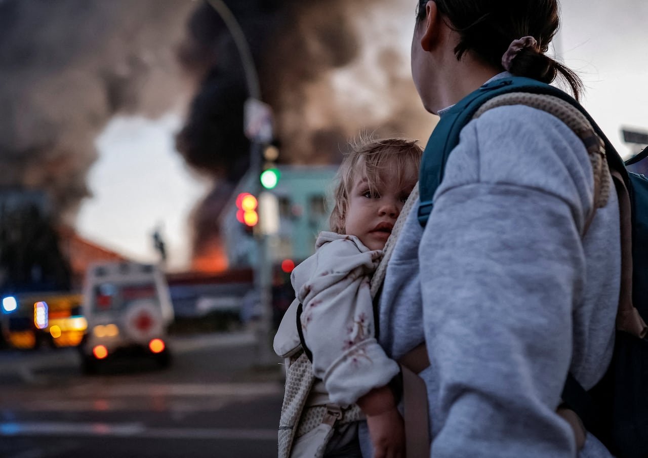 A woman with a baby in front of a burning building.