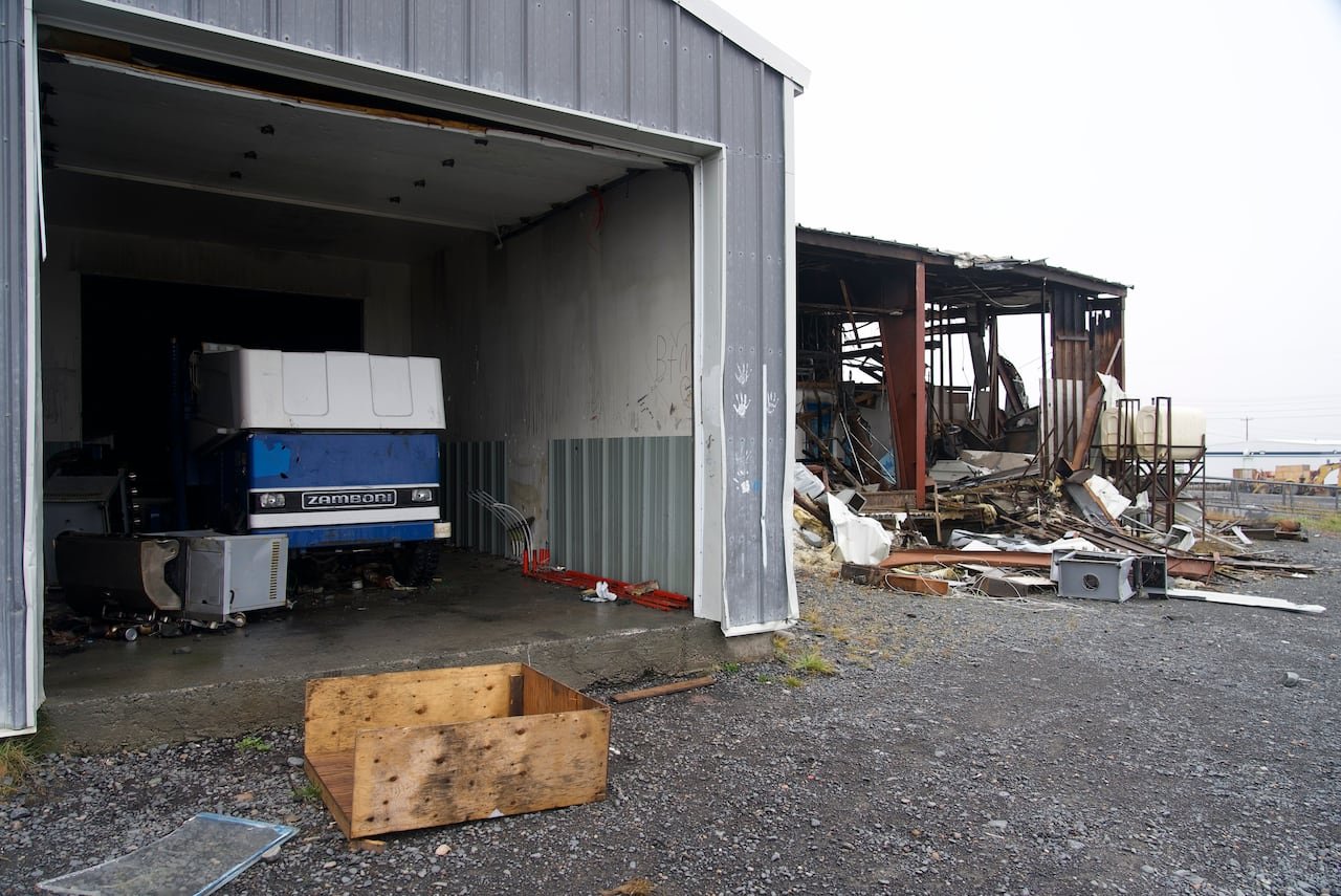 A Zamboni in a garage-like structure, connected to a partially damaged building.